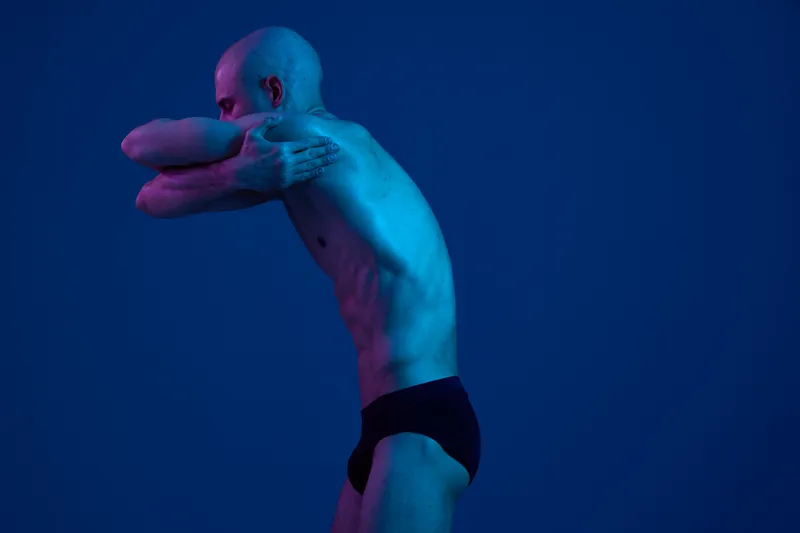 A fit man striking a dynamic pose against a dark blue background, showcasing the beauty of the human form through vibrant colors and contrast.