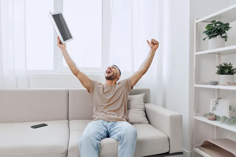 Excited man celebrating a career pivot, showcasing joy and relief in a cozy home setting. Emphasizes themes of personal growth and emotional minimalism.