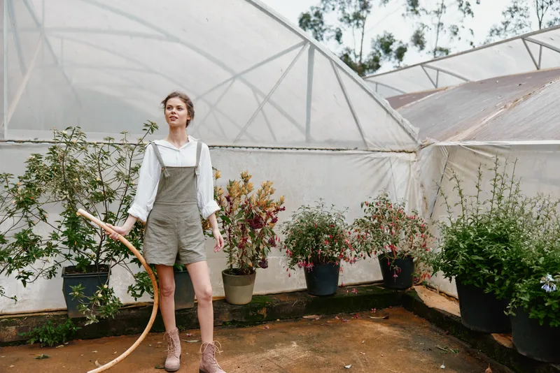 Female model in overalls surrounded by lush plants in a greenhouse, showcasing gardening passion and serene emotions during spring
