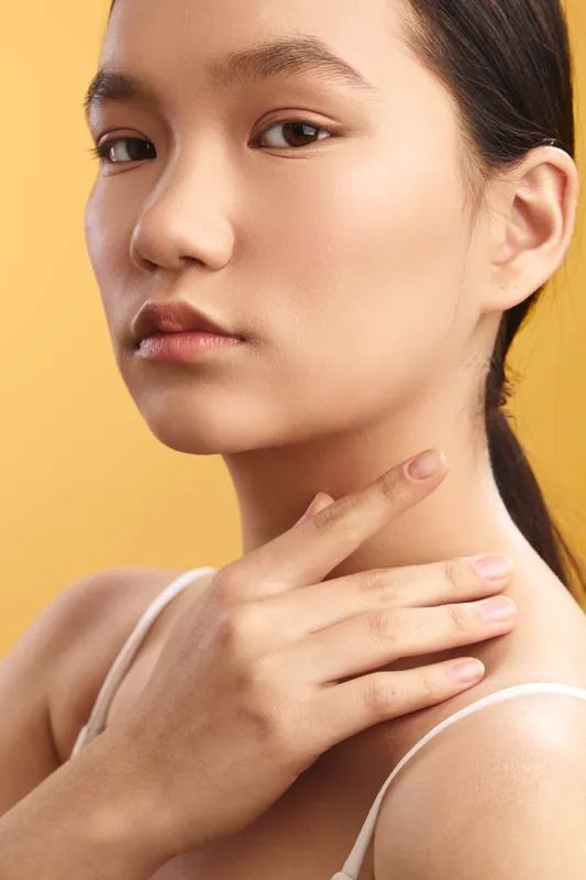 Asian woman with serene expression in a close up portrait against a warm backdrop, highlighting smooth skin, soft lighting, and a graceful, poised pose.