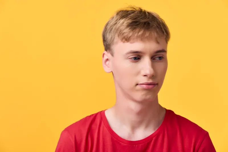 Young man wearing a red shirt against a bold yellow background, relaxed posture, soft lighting, and a minimal studio setting for lifestyle or fashion use.