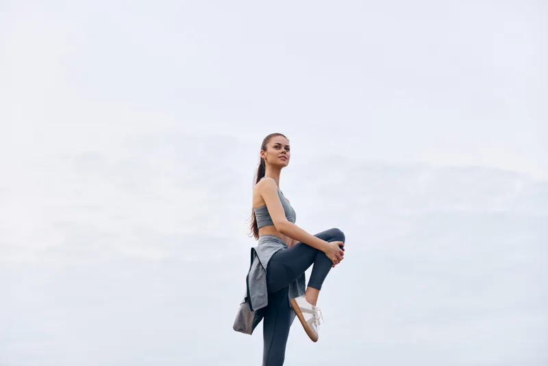 Confident young woman in athletic wear performing a stretch outdoors, showcasing fitness and strength in a gray atmosphere