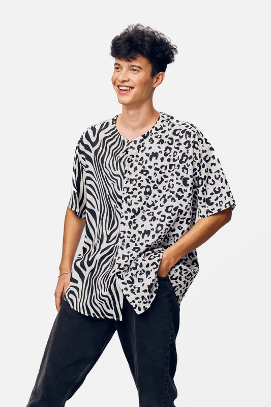 young man wearing black and white animal print shirt laughing with casual black pants on plain white background, cheerful expression, modern fashion style.