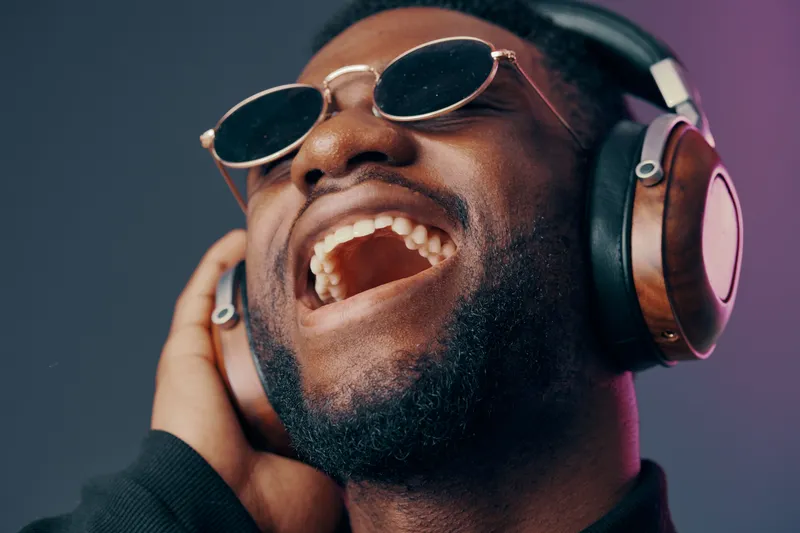 Joyful African man with headphones enjoying music, wearing sunglasses, in vibrant colors with a cool background, representing happiness and music culture