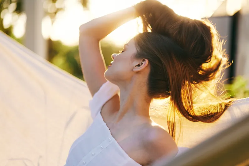 A serene woman with flowing hair enjoying the warm sunlight, showcasing healthy hair and a tranquil outdoor setting with soft colors
