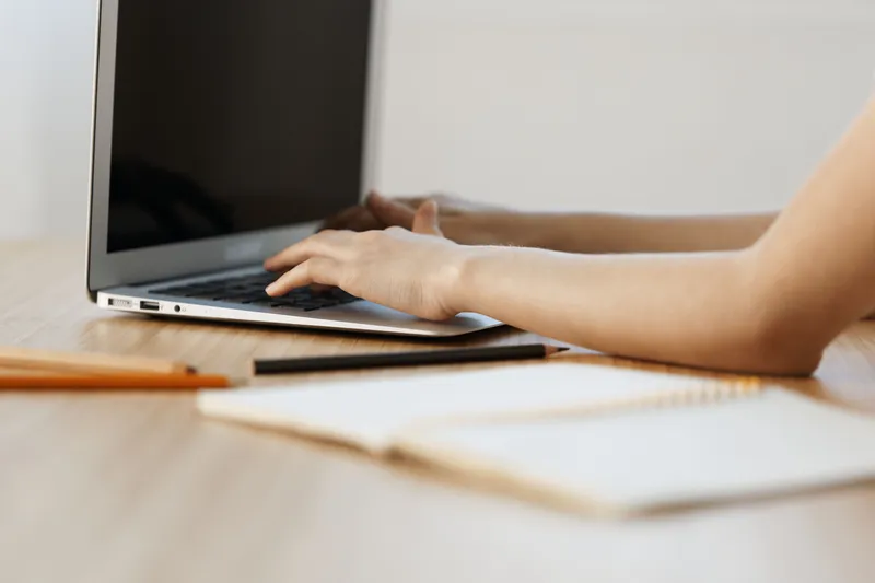 Young woman typing on a laptop at a wooden desk, showcasing focus and productivity in a modern workspace, emphasizing the concept of remote work and digital communication