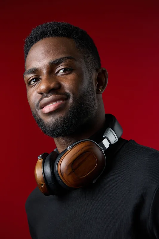 Young Black man with headphones on a red background, showcasing confidence and modern style, perfect for technology and lifestyle concepts