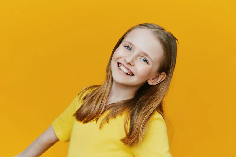 Happy young girl with braces smiling in a bright yellow shirt against a vibrant yellow background, expressing joy and positivity, perfect for children s themes