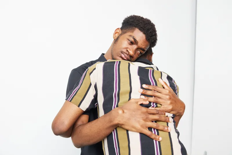 Two African American men share an emotional embrace, highlighting their bond and support for one another. Their expressions convey deep feelings of care and connection.