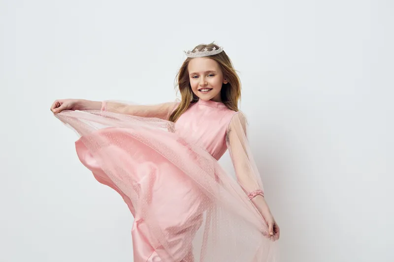 A joyful young girl wearing a pink dress and crown, spinning gracefully against a light background, capturing the essence of childhood and elegance