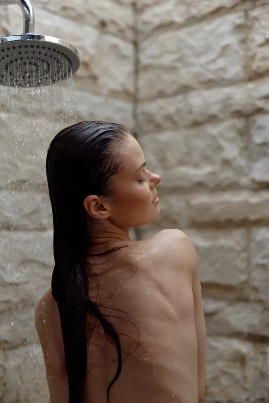 young woman enjoying outdoor shower with wet hair against natural stone wall, serene and relaxed mood on a warm day