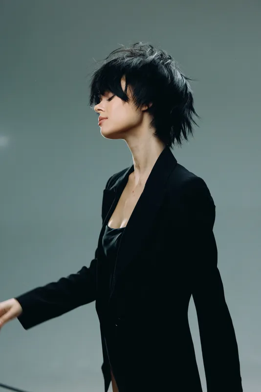Stylish woman with short black hair wearing a black blazer in a minimalistic studio setting