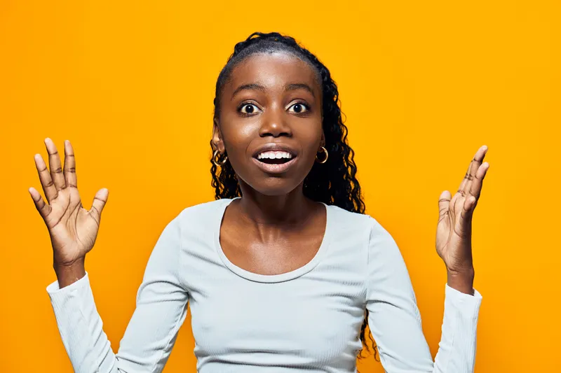 Excited young African woman expressing surprise and joy against a bright yellow background, showcasing vibrant emotions and a casual style