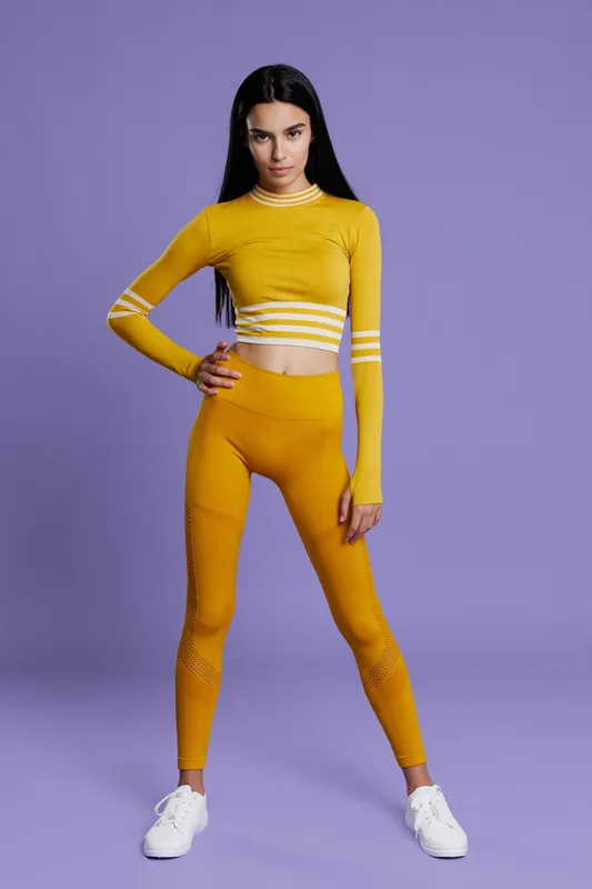 Woman sport fitness wearing stylish yellow athletic outfit, standing confidently against purple background, showcasing health, strength, and active lifestyle.