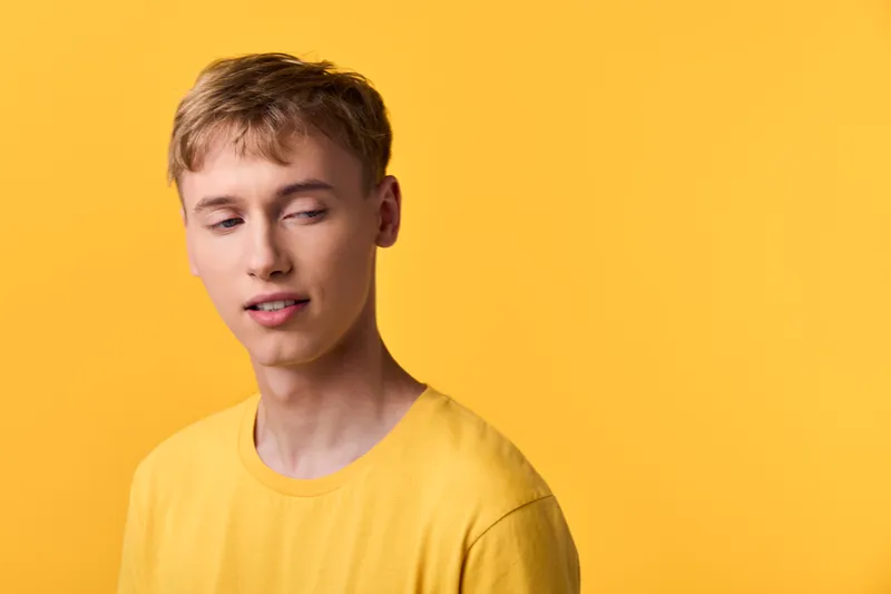 Young man in a yellow shirt against a yellow background with a relaxed casual mood and sleepy facial expression, studio headshot for lifestyle and fashion