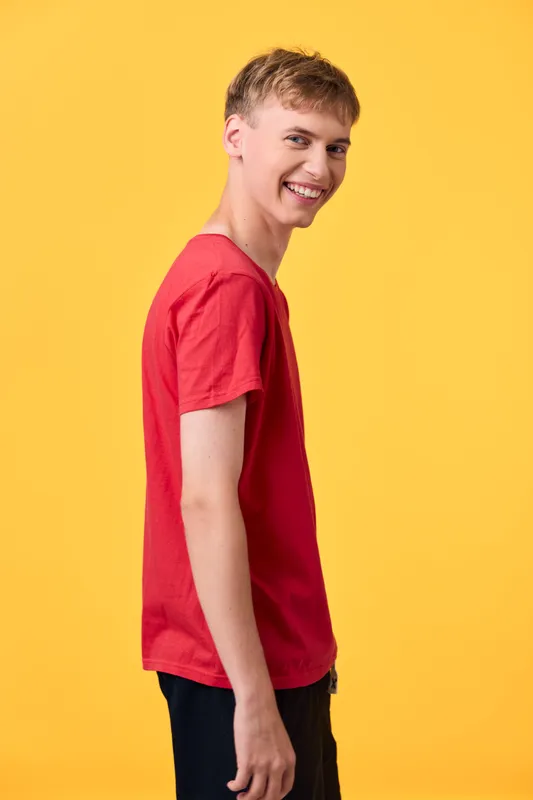 Smiling young man in a red t shirt poses against a bright yellow background, casual studio shot with a friendly expression and vibrant color for lifestyle content