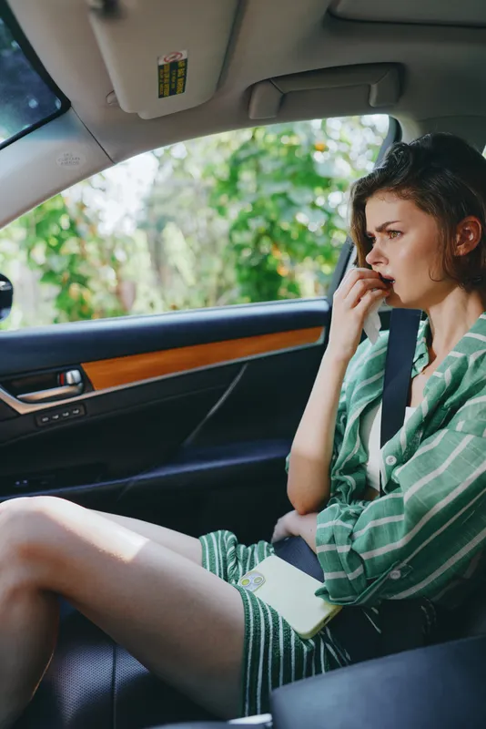 Young woman sits in a car wearing a seatbelt, talking on her phone, lost in thought during a quiet, reflective drive.
