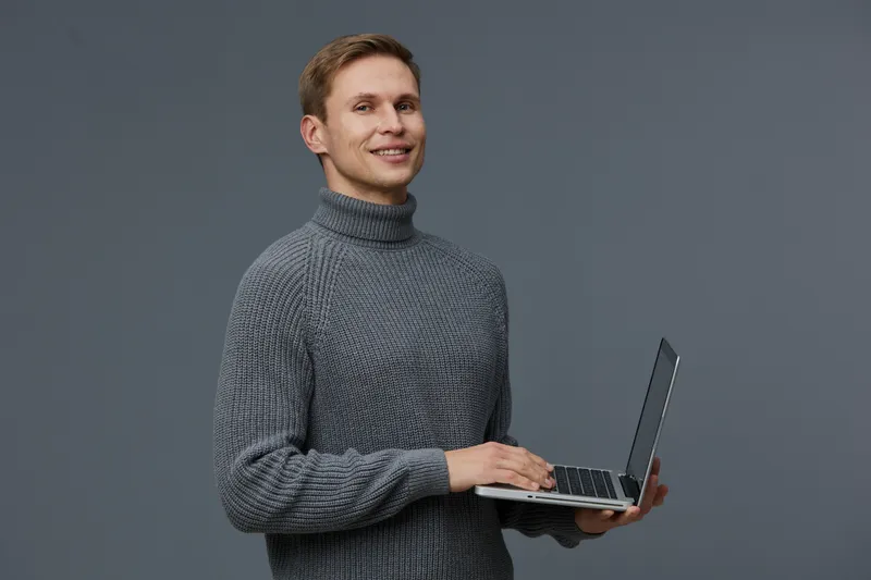 smiling man holding laptop wear gray knitted turtleneck sweater look camera isolated on gray background digital nomad technology concept