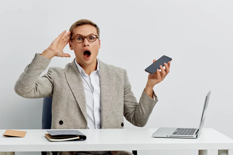 surprised man using smartphone work laptop digital detox concept casual wear glasses modern office light background