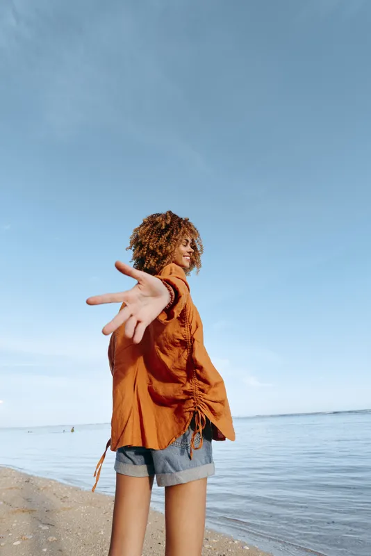 Mother child beach ocean summer outdoors curly woman happiness family on sandy shoreline under clear blue sky, adult with curly hair holds a toddler close, smiling, enjoying gentle sea breeze, calm