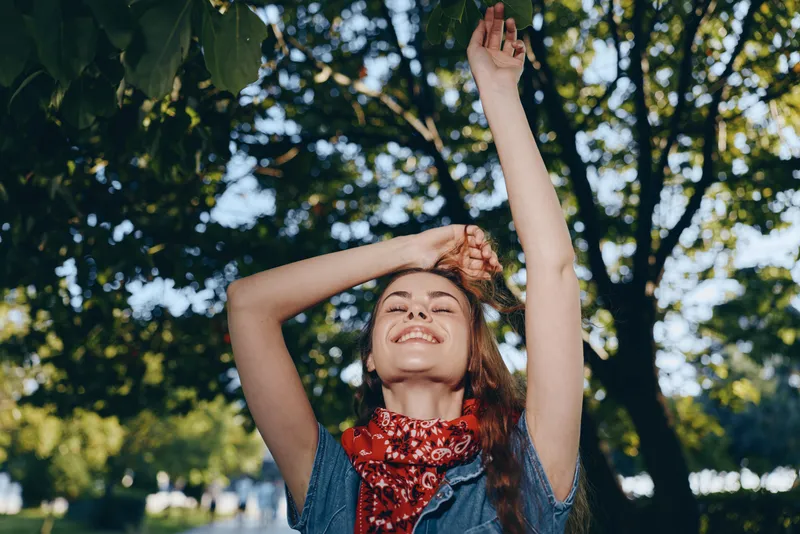 Lifestyle woman wearing modern boho-western denim street style with a red bandana, enjoying sunlight outdoors, captured with warm film color tones.