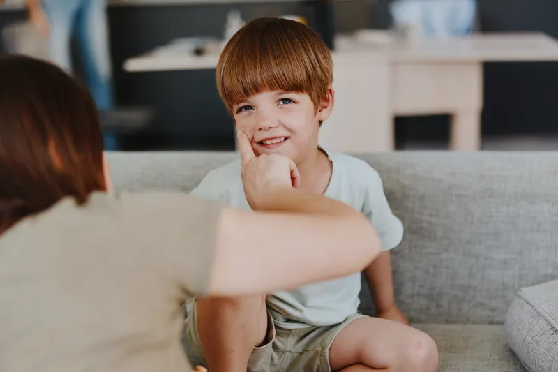 Joyful boy enjoying playful moment with mother, cozy indoor setting, bright colors, heartfelt connection captured in a warm atmosphere.