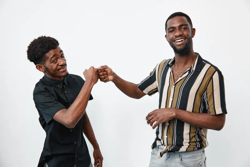 Two young black men with dark skin fist bumping and smiling in casual clothes on white background. Friendship, happiness and positive connection between african american friends.
