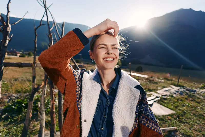 Woman smile mountain sunlight jacket portrait outdoors happy traveler enjoying scenic landscape, wearing warm patterned coat and denim shirt, candid closeup with sunflare and natural background.