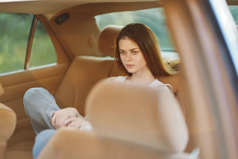 Young woman with long brown hair sitting thoughtfully in a car, wearing casual clothing, reflecting emotions of contemplation and serenity in a warm interior.