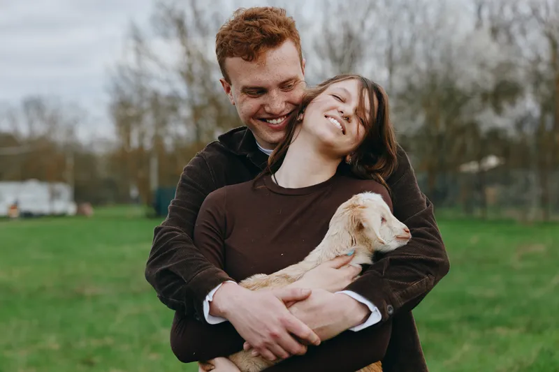 Happy couple outdoors embraces a dog, smiling warmly in a green park, conveying affection, companionship, and a relaxed lifestyle as they enjoy playful moments together under soft daylight.