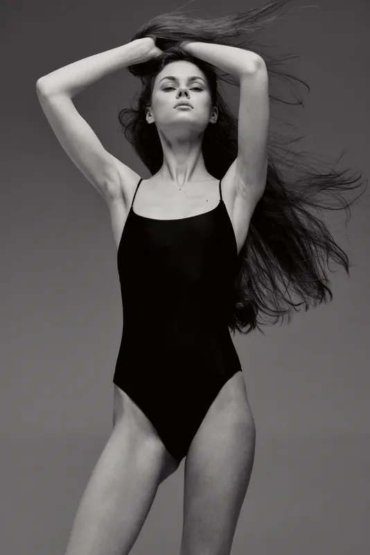 Black and white portrait of a woman in a black bodysuit posing confidently with flowing hair and strong expression.