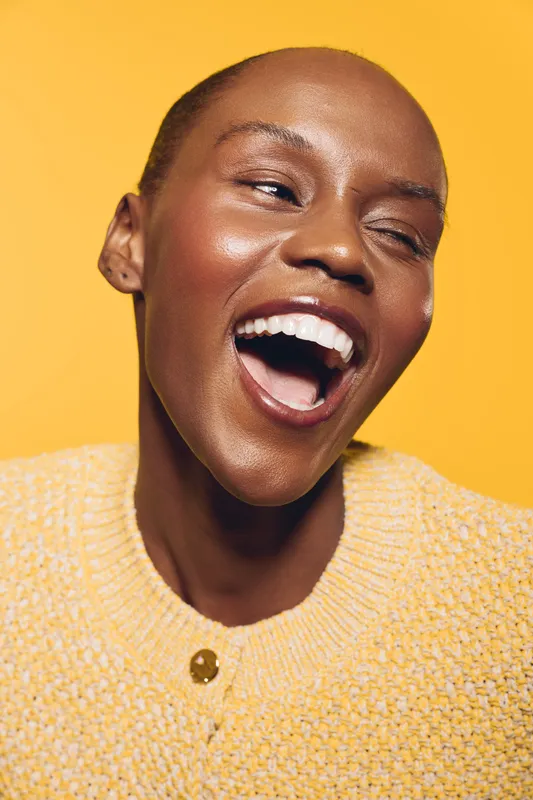 Close-up of a happy African woman with dark skin laughing joyfully against yellow background. Concept of happiness, beauty, and natural skin glow in portrait photography.