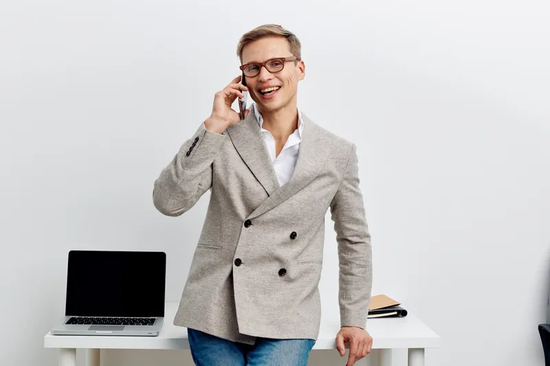 smiling man talking phone casual business jacket glasses standing laptop desk remote work digital nomad concept