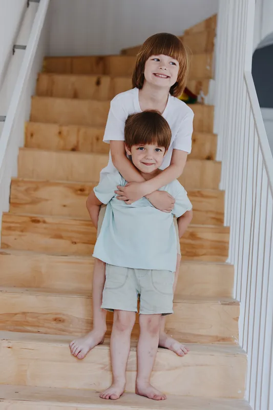 Happy children playing on wooden stairs, enjoying a joyful moment together with smiles and laughter in a bright home setting.