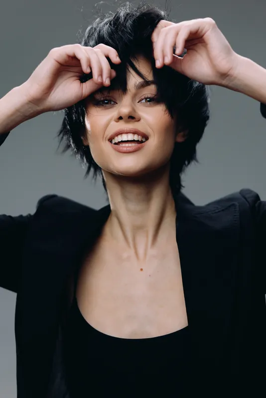 smiling woman with short black hair wearing stylish black jacket expressing joy in studio