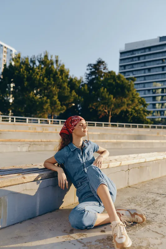 Lifestyle woman in modern boho-western denim street style relaxing outdoors with casual outfit and red bandana, captured with warm film color tones.