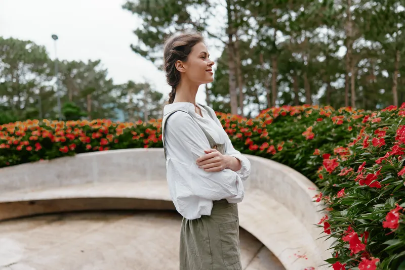 Young woman in a serene posture among vibrant flowers, wearing a casual outfit, exuding tranquility and confidence in a natural setting