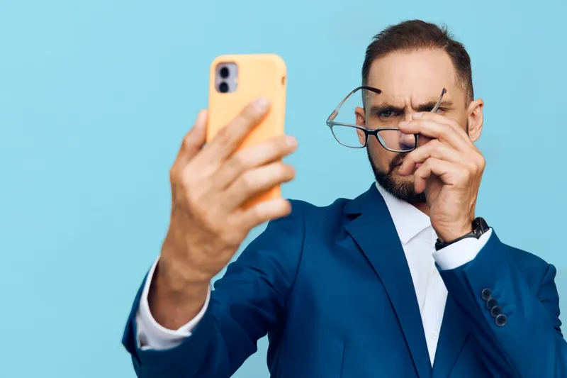 A focused businessman in a blue suit studies a smartphone, isolated against a vivid blue backdrop, conveying confidence, focus, and professional emotion.
