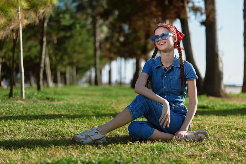 lifestyle woman in modern boho-western denim street style sitting on grass outdoors with film color tone, smiling and relaxed in sunny natural setting