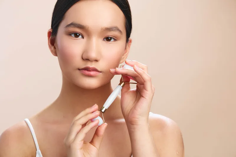 Asian woman carefully applies lipstick in a soft studio setting, presenting poised makeup artistry and confident focus, with even lighting, clean background, and serene mood.