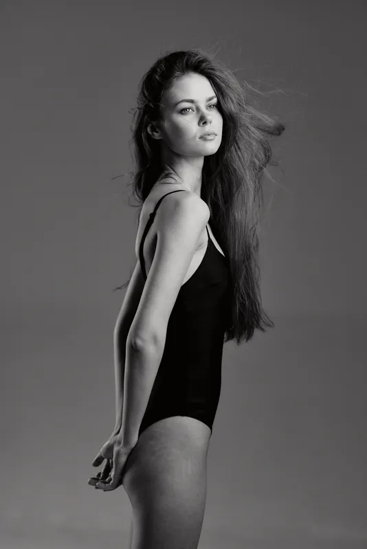 Black and white portrait of a young woman with flowing hair wearing a black bodysuit expressing calmness and elegance.