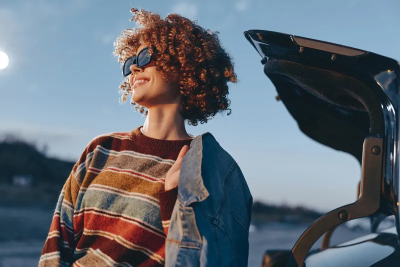 Woman lifestyle, curly hair, smiling outdoors, striped sweater, denim jacket, bicycle handle closeup, sunny travel mood, natural light, lifestyle concept with copy space