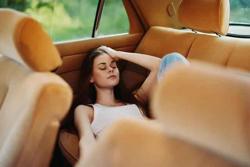 Young woman relaxing in a vintage car with a serene expression, surrounded by soft orange upholstery, capturing a sense of calm and nostalgia.