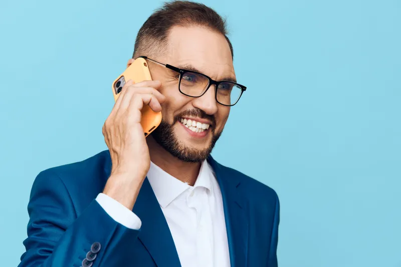 A professional man in a blue suit speaks on a smartphone against an isolated colorful background, expressing confident emotion and approachability, suitable for corporate marketing and business