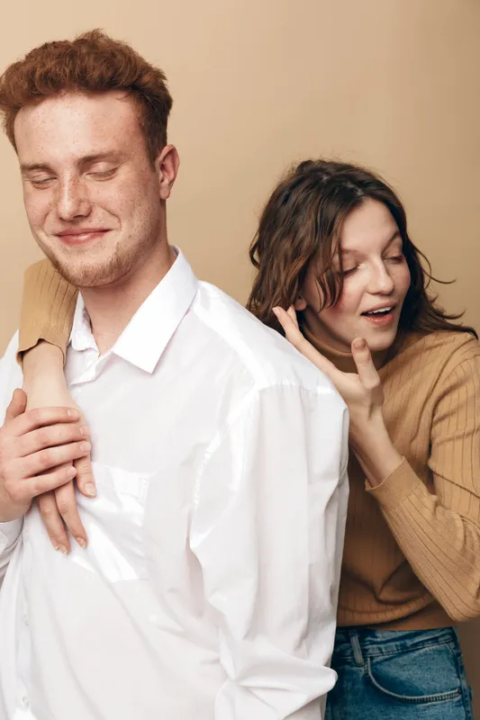 Young man and woman in casual clothes share a playful moment, woman whispering to man with closed eyes. Concept of friendship, communication, and happiness.