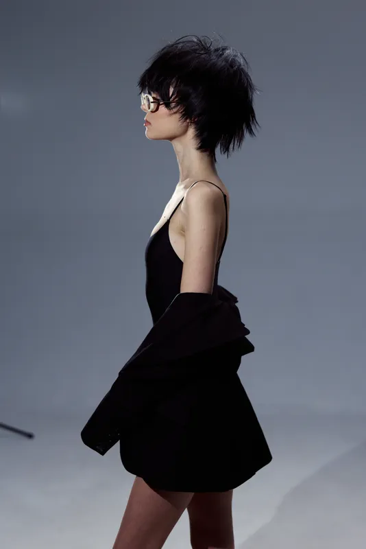Profile of a stylish woman wearing glasses and black clothing with short hair against a neutral background.