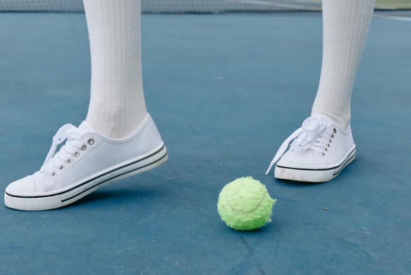 Young athlete in white sneakers and knee high socks engaging in tennis, showcasing excitement and energy on a vibrant court with a neon green tennis ball