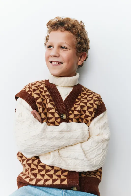 Authentic portrait of a young boy in a cozy knit vest, capturing simple charm, hopeful smile, and a genuine moment that reflects everyday school life and light play.