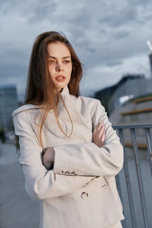 confident woman with crossed arms wearing stylish light beige jacket urban outdoor portrait cloudy sky fashion business concept