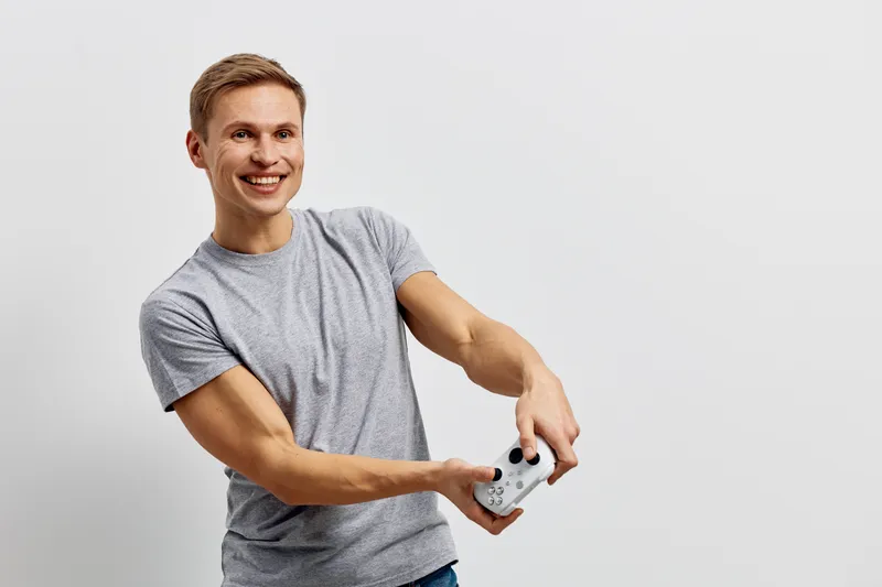 Smiling young caucasian man play game hold wireless controller wear gray t-shirt isolated on light background concept digital detox and mental health with gadgets